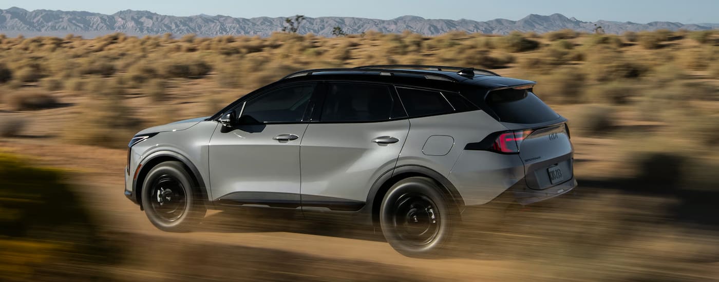 Rear of a grey 2026 Kia Sportage driving off-road.