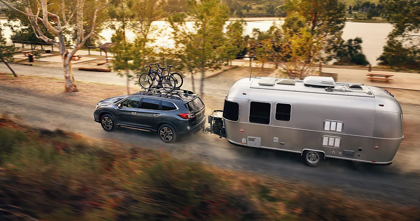 Subaru Ascent with bikes on the roof towing a travel trailer along a lakeside road