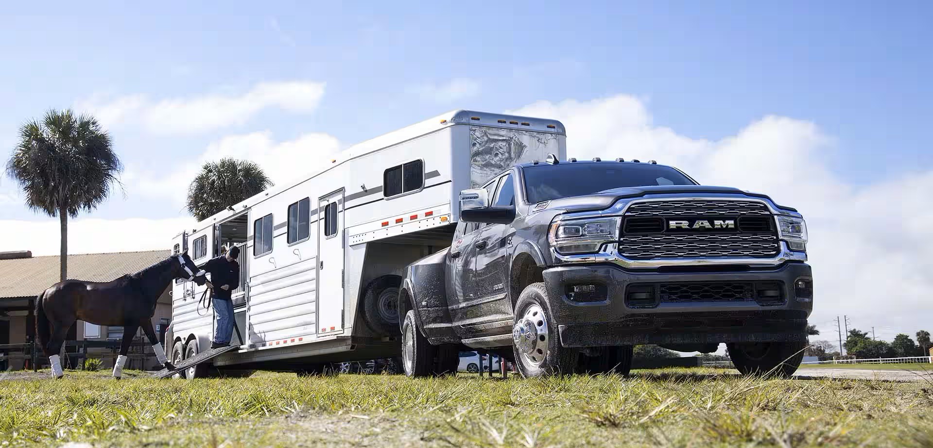 A man walking a horse into a trailer attached to a black truck.