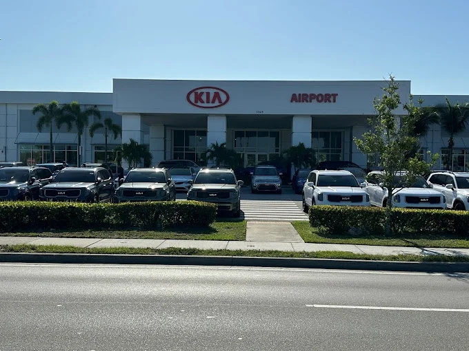 Exterior of Airport Kia of Naples dealership with vehicles parked in the front lot under a clear blue sky