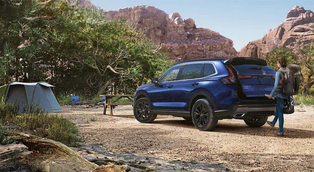 A family is getting camping gear from the back of a blue 2025 Honda CR-V Sport Touring Hybrid.