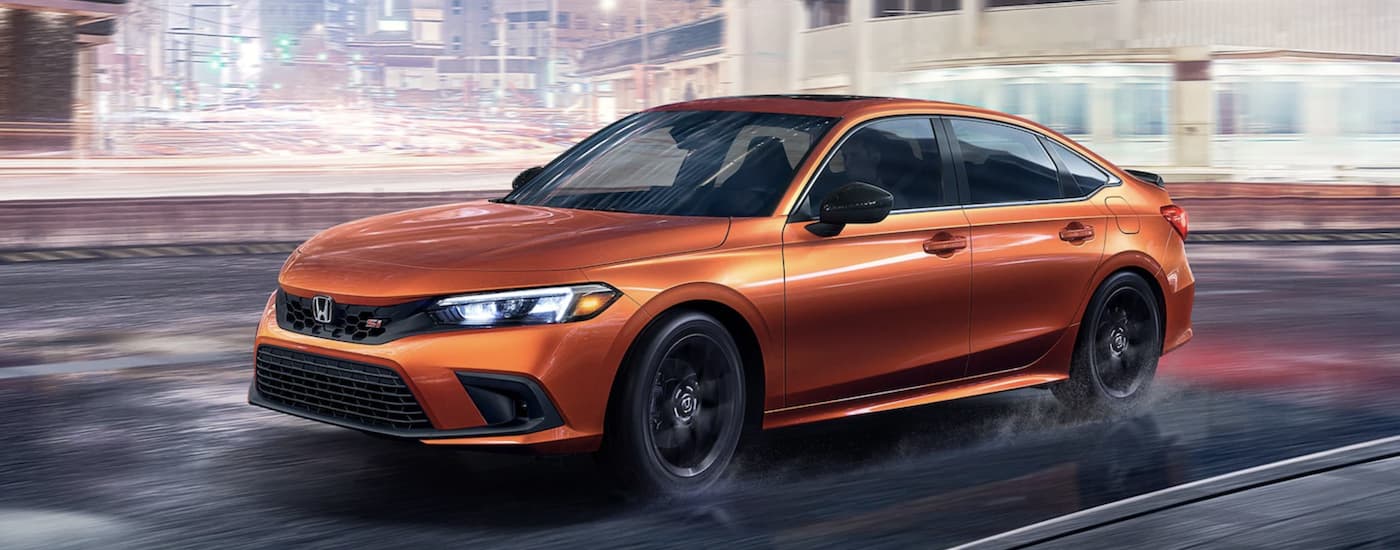 An orange 2022 Honda Civic Si is shown driving through a city.