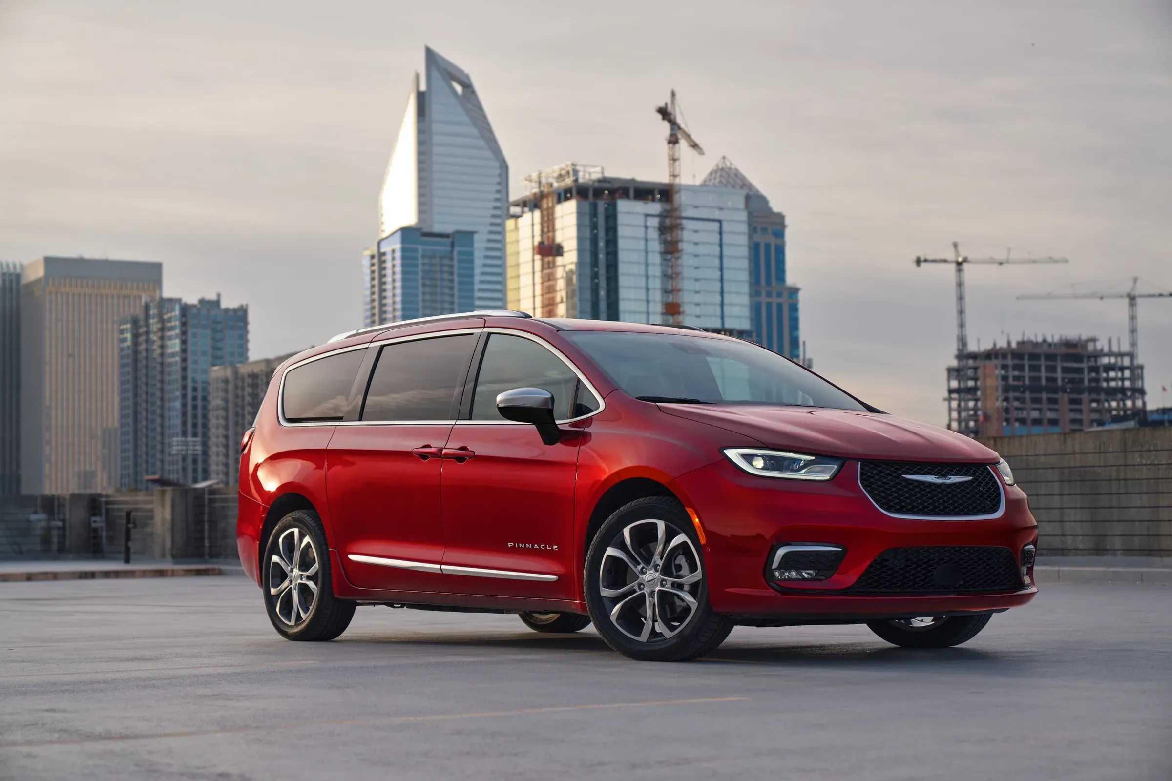 2026 Red Chrysler Pacifica Pinnacle minivan parked on a rooftop lot with city high-rises and a construction crane in the background