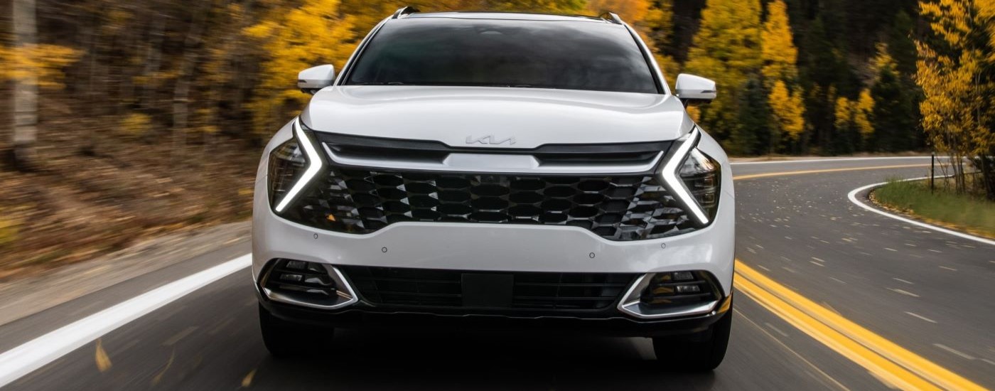 Front of a white 2023 Kia Sportage Hybrid driving down a road