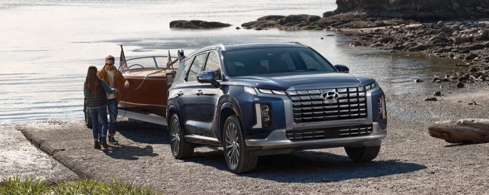 Couple walking toward a 2025 Hyundai Palisade towing a wooden boat by the water