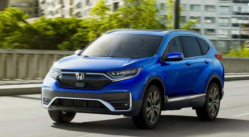 Blue 2020 Honda CR-V Touring is driving on a city street near Rochester, NY