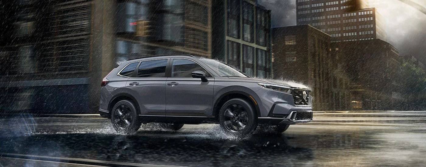 A grey 2023 Honda CR-V is shown from the side driving through a city on a rainy day.