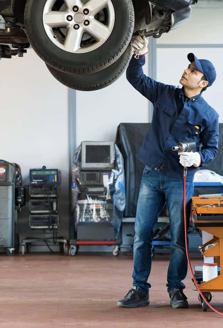 auto technician makes repairs to car on lift
