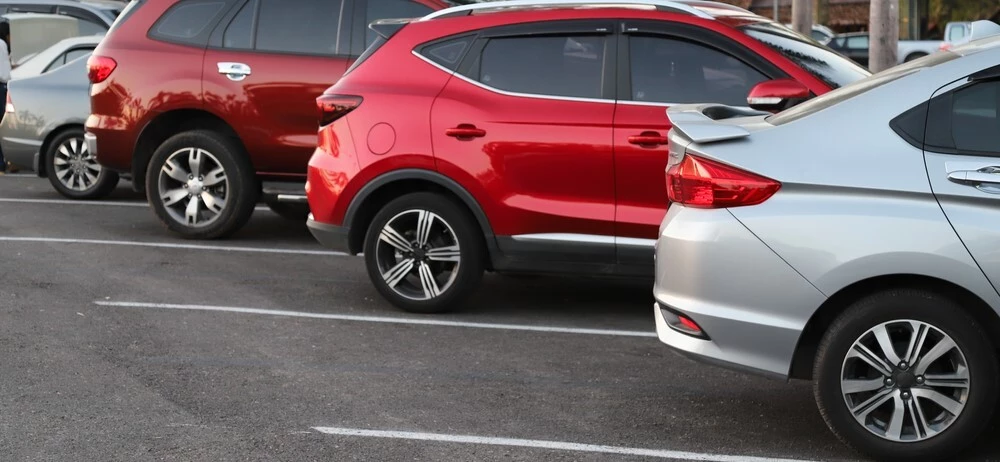 4 Cars are visible in frame in a parking lot, a silver car is first followed by two red cars, behind those 3 is another silver car, all the spots are on a diagonal