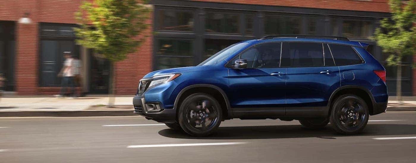 A blue 2021 Honda Passport Elite is shown from the side in front of a brick building.