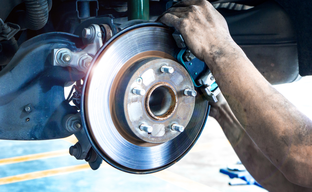 A Mechanics hands are visible in the image, working on a cars brake, the arms are covered in soot and grime