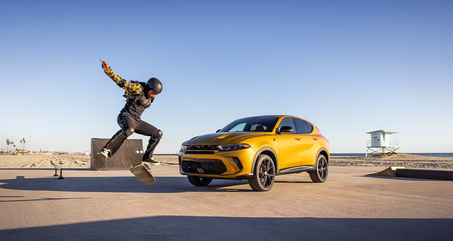 Man skating next to a yellow dodge hornet.