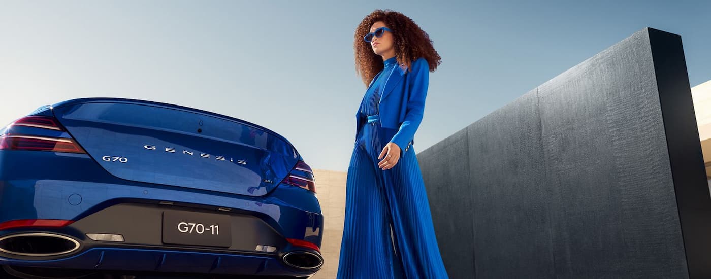 Woman walking near the back of a blue 2026 Genesis G70