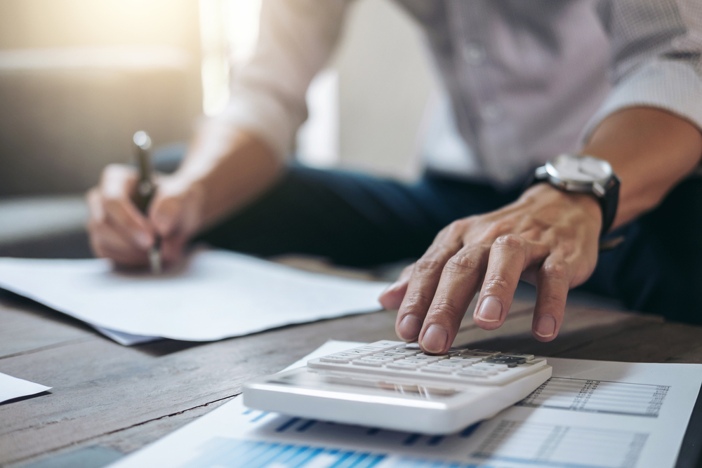 man uses calculator while taking notes; focus on hands, no face shown