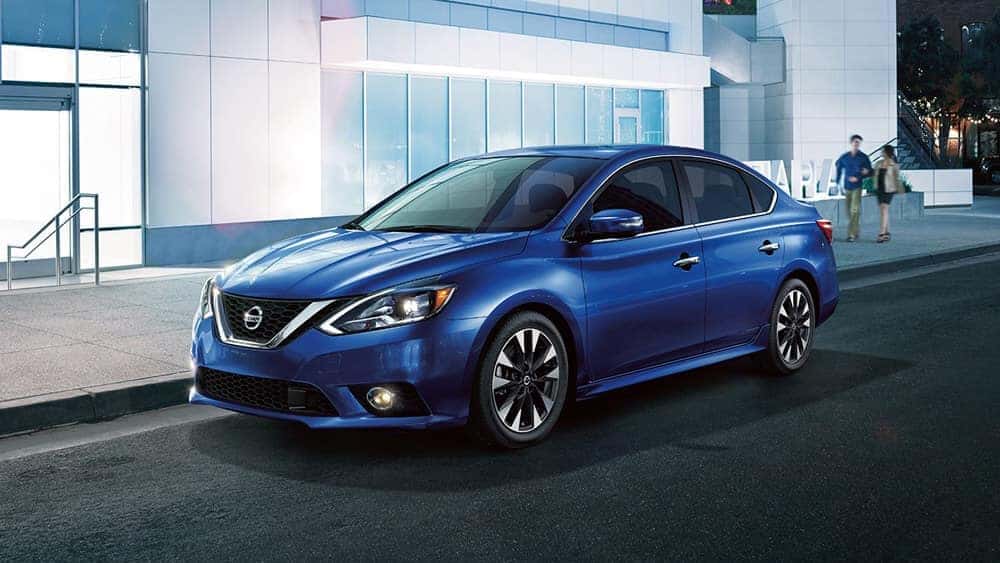 Blue 2018 Nissan Sentra sedan parked in front of a modern glass building