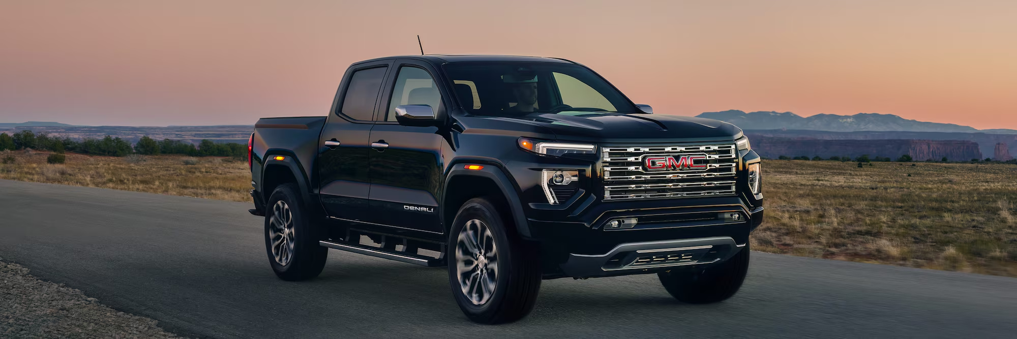 Black GMC Canyon Denali driving on a desert highway at sunset