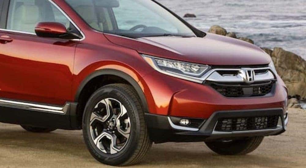A red 2018 Honda CR-V is shown driving on a highway near an ocean.