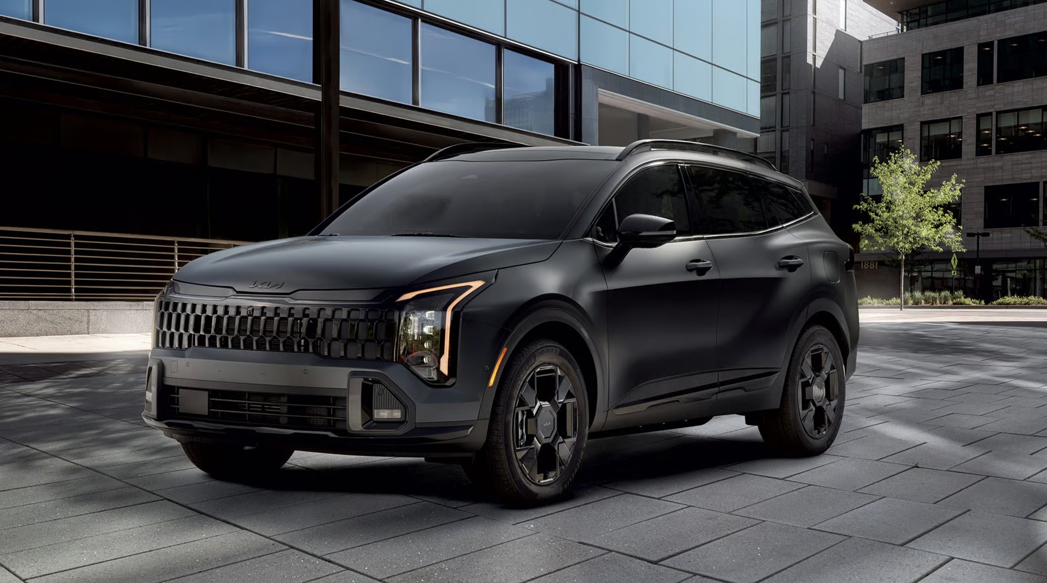 Matte black 2027 Kia Sportage plug-in hybrid SUV parked on a paved plaza in front of a modern glass office building, shown from a front three-quarter angle.