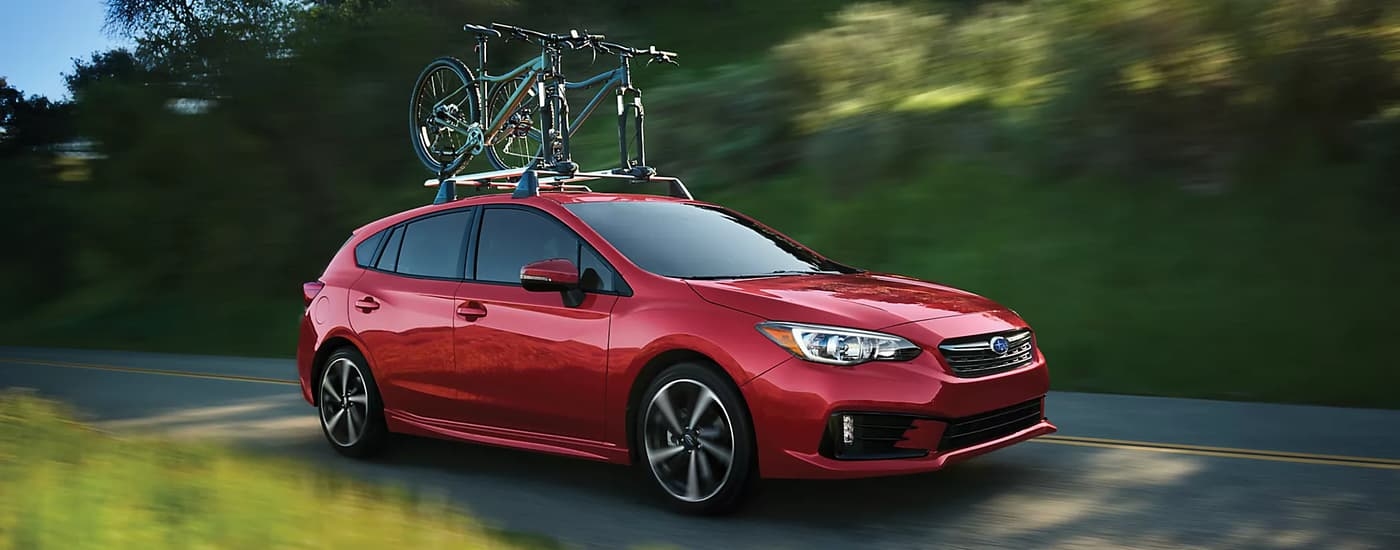 A red 2023 Subaru Impreza Sport is shown driving on a tree-lined road after leaving a Subaru dealership in Red Hook.
