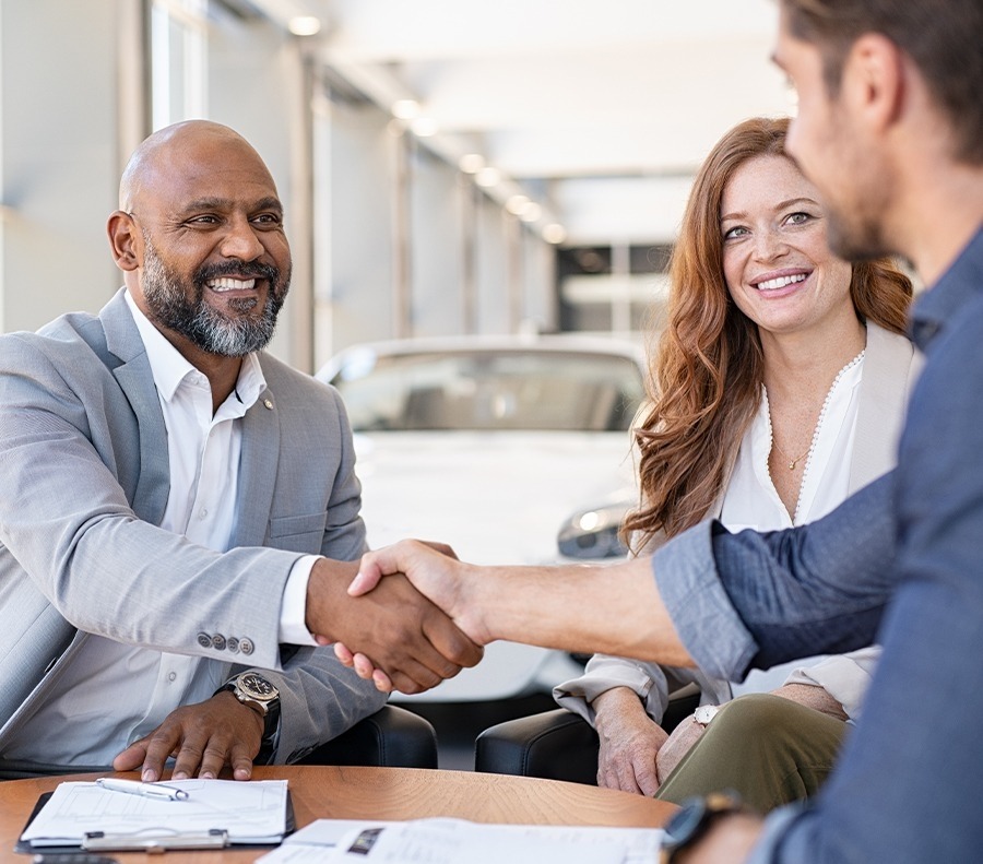 Salesperson shaking hands with a smiling couple in a dealership showroom