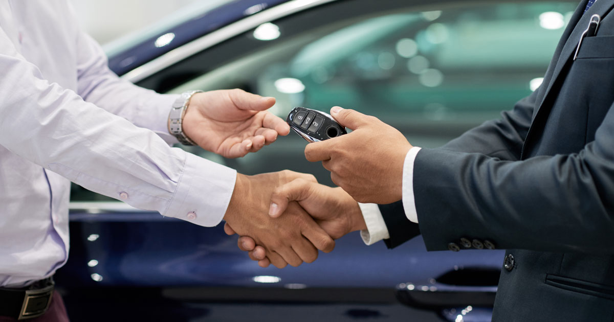 A car salesman hands a customer a set of keys to their new car.