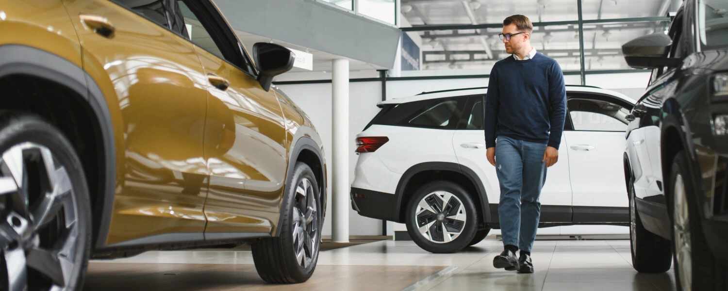 A shopper examines used SUV vehicles dealership showroom, with white and black SUVs displayed nearby.