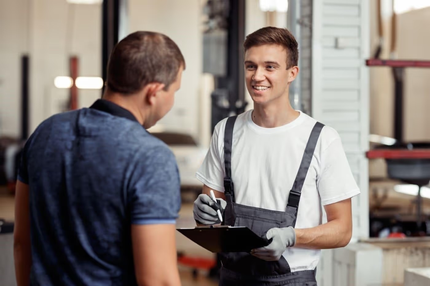 Service technician with a clipboard talking with a customer in the service bay