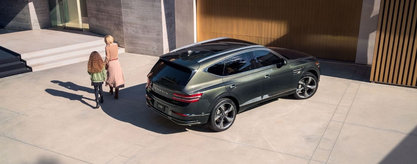 Two people walking near a green 2025 Genesis GV80