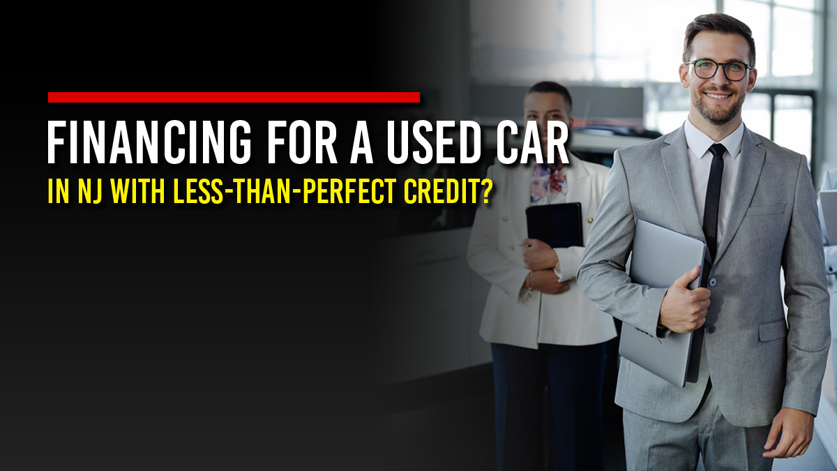 Smiling car dealership finance manager in a gray suit holding a laptop, with a colleague behind him in the showroom, next to the headline “Financing for a Used Car in NJ with Less-Than-Perfect Credit?"