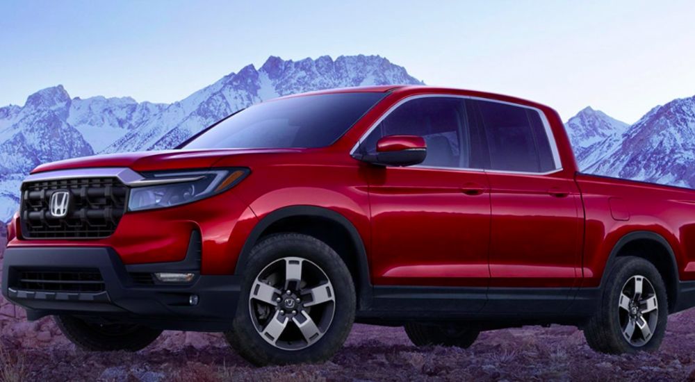 Red 2026 Honda Ridgeline parked off-road with mountains in the background.