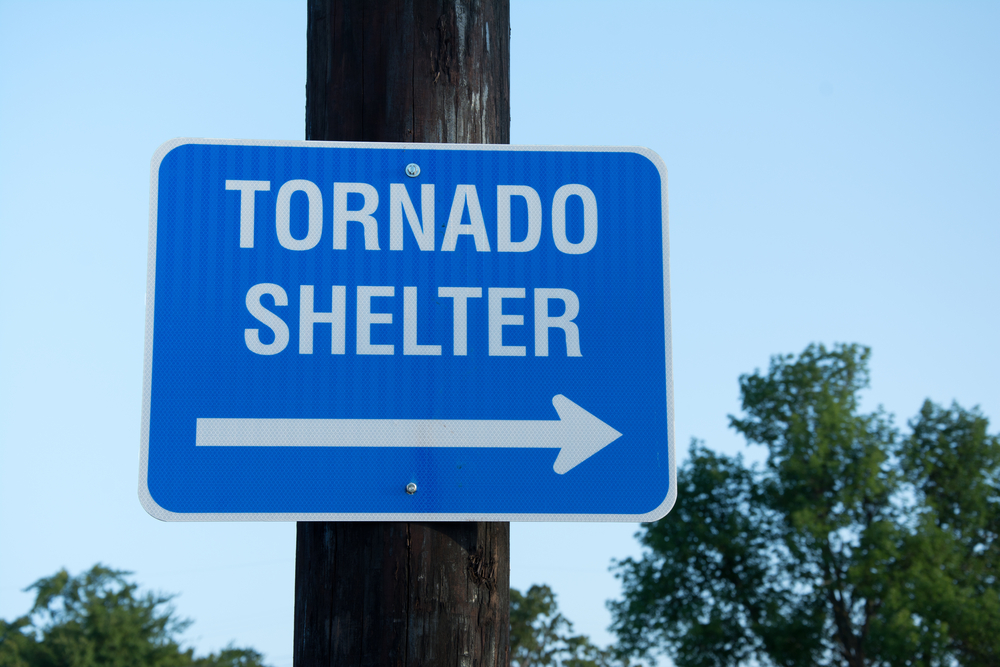 a pole with a blue and white tornado shelter sign that has an arrow pointing in the direction of a tornado shelter