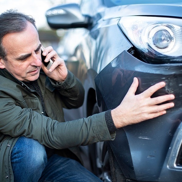 Driver on the phone inspecting a dented car fender after a collision