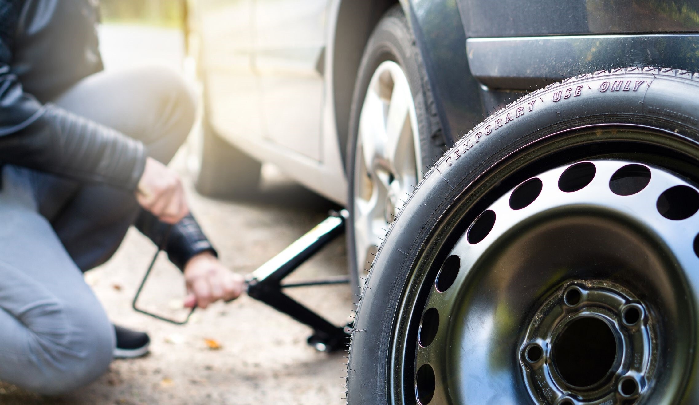 Technician using a jack to change a tire beside a spare wheel