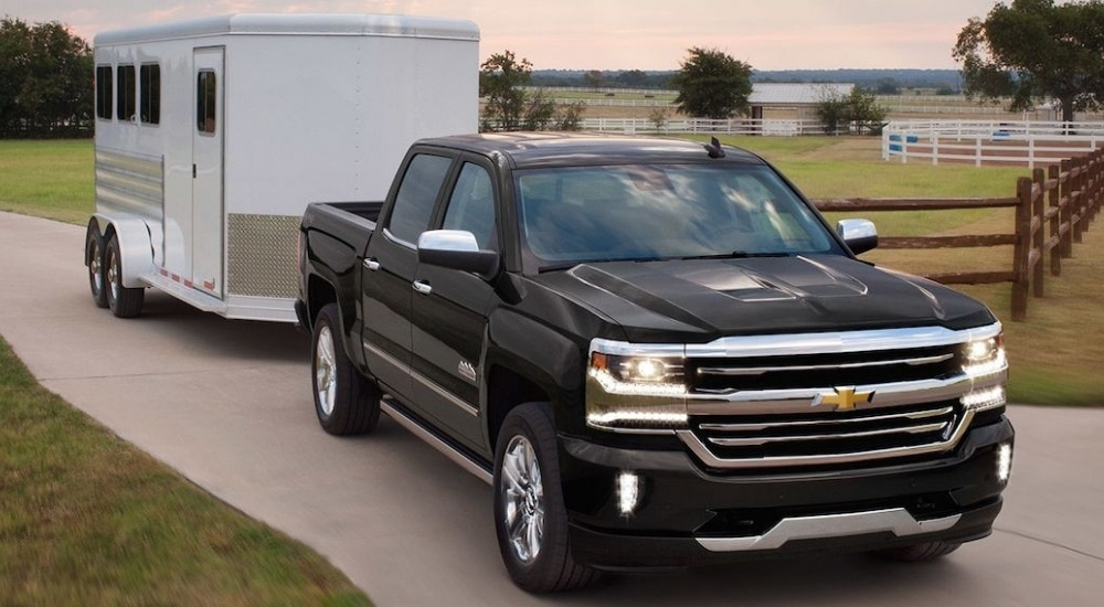 Black 2018 Chevy Silverado 1500 towing a white trailer on a farm