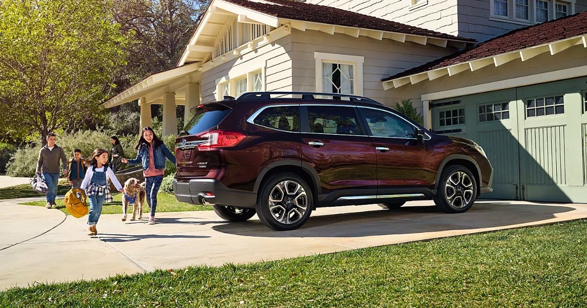 Family and their dog walking toward a maroon Subaru Ascent parked in a home driveway