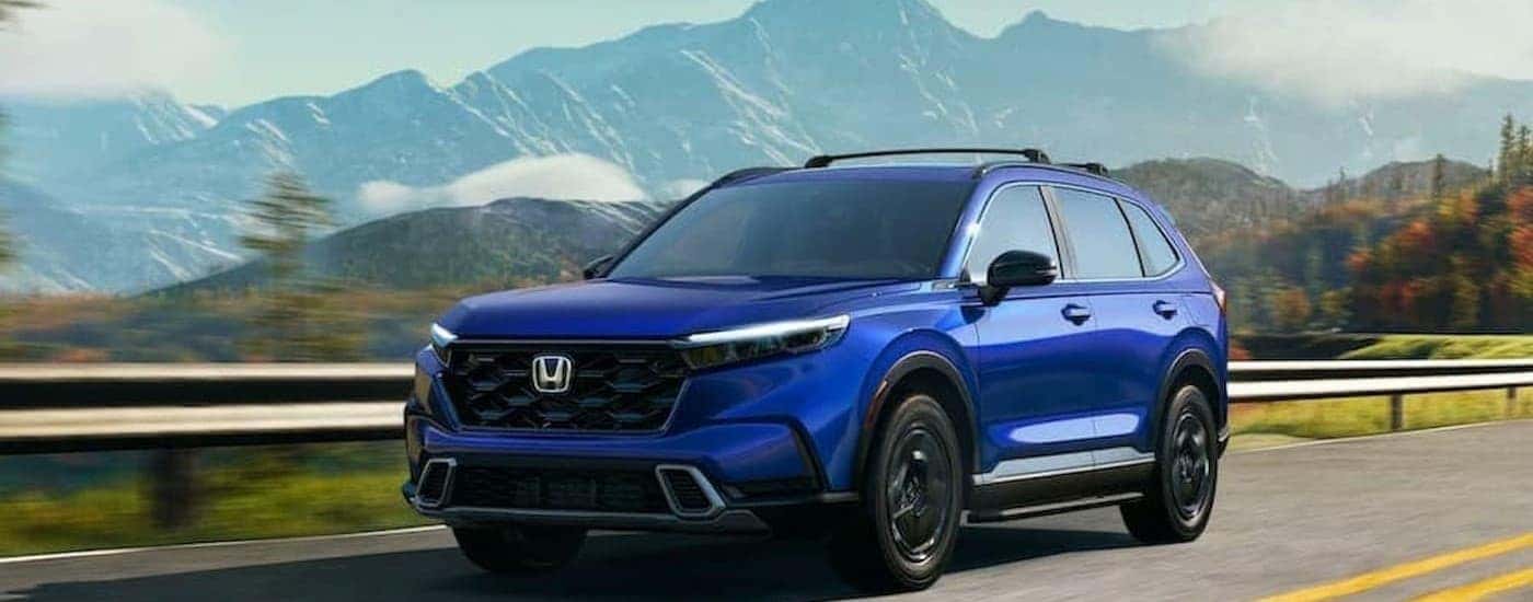 A blue 2025 Honda CR-V Hybrid Sport Touring driving on a highway.