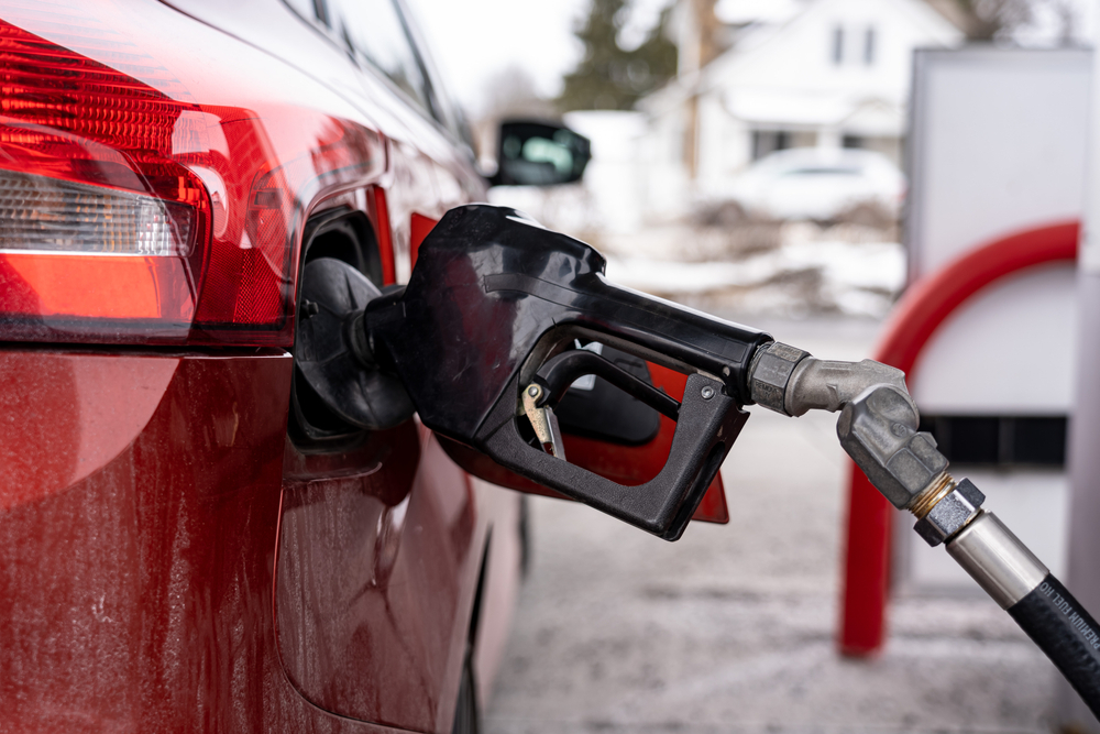 In focus is a black gas nozzle filling up a red car