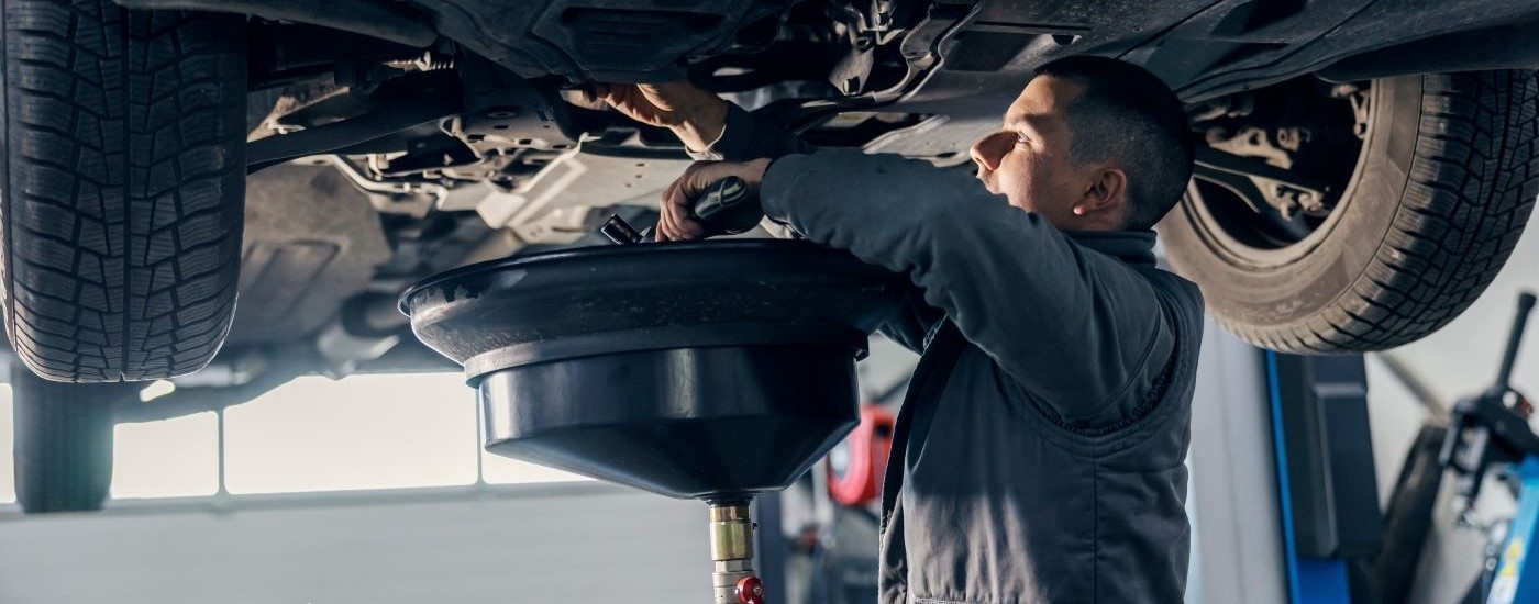  A mechnic is shown uder a vheicle on a lift during an oil change near you.