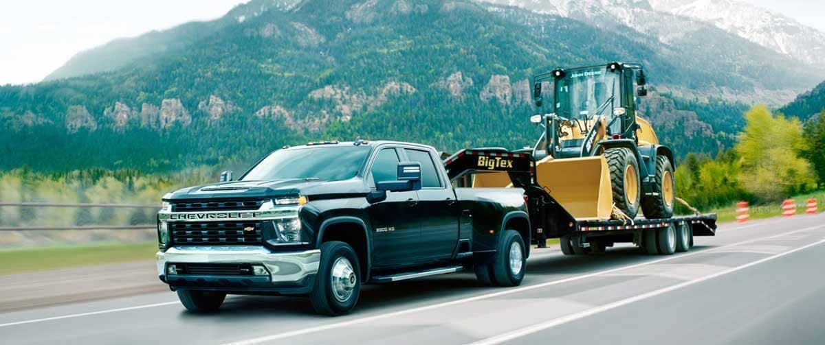 A black Chevrolet Silverado 3500 towing a front scooper on a big tex tower through a highway on a montainous road.