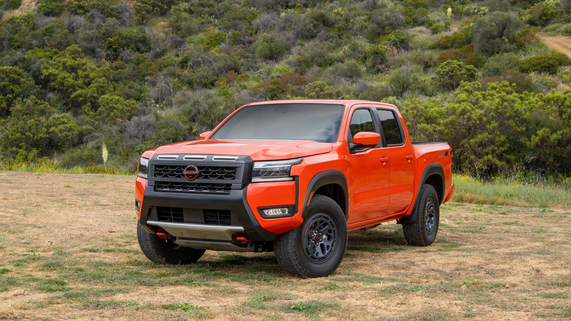 2026 Nissan Frontier® orange pickup truck parked off-road with black grille and all-terrain tires