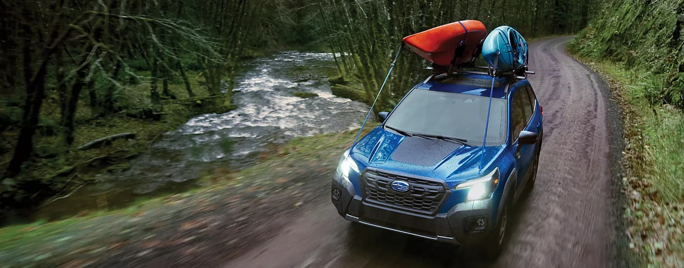 A blue 2023 Subaru Forester Wilderness with kayaks on top.