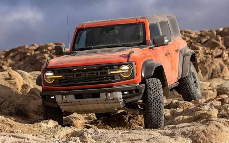 image of orange ford bronco raptor driving over rough terrain