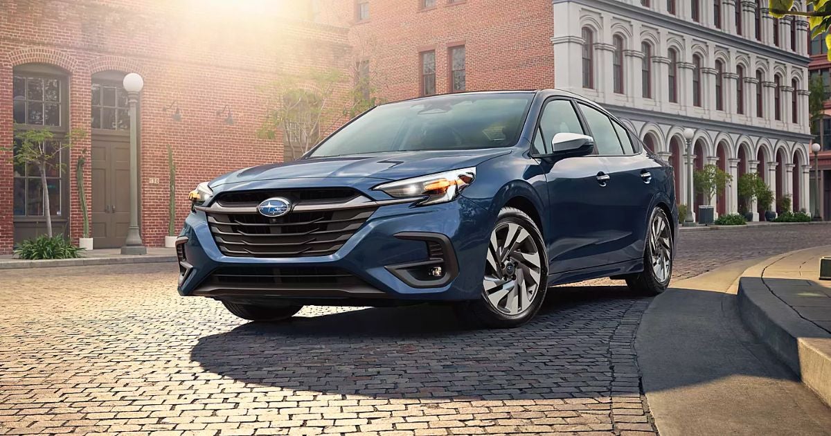 Blue 2025 Subaru Legacy sedan parked on a cobblestone street lined with brick buildings