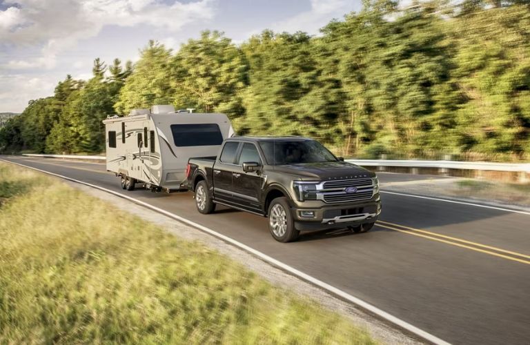 Green 2024 Ford F-150 Towing a Camper on a Country Highway