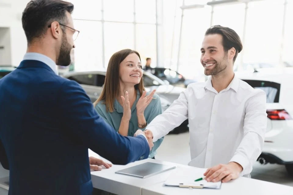 Salesperson shaking hands with a smiling couple at the finance desk after completing a Kia financing agreement