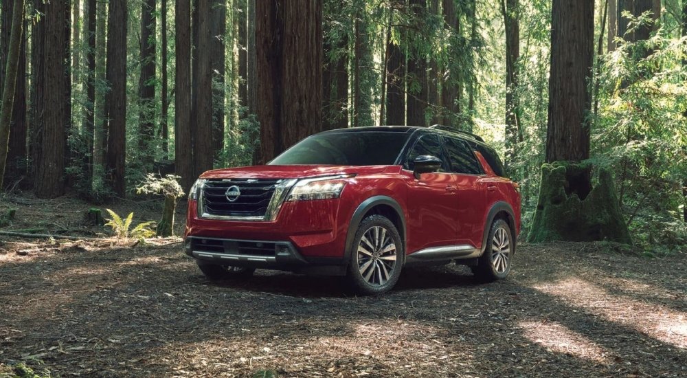 Red 2025 Nissan Pathfinder parked in a woodland clearing