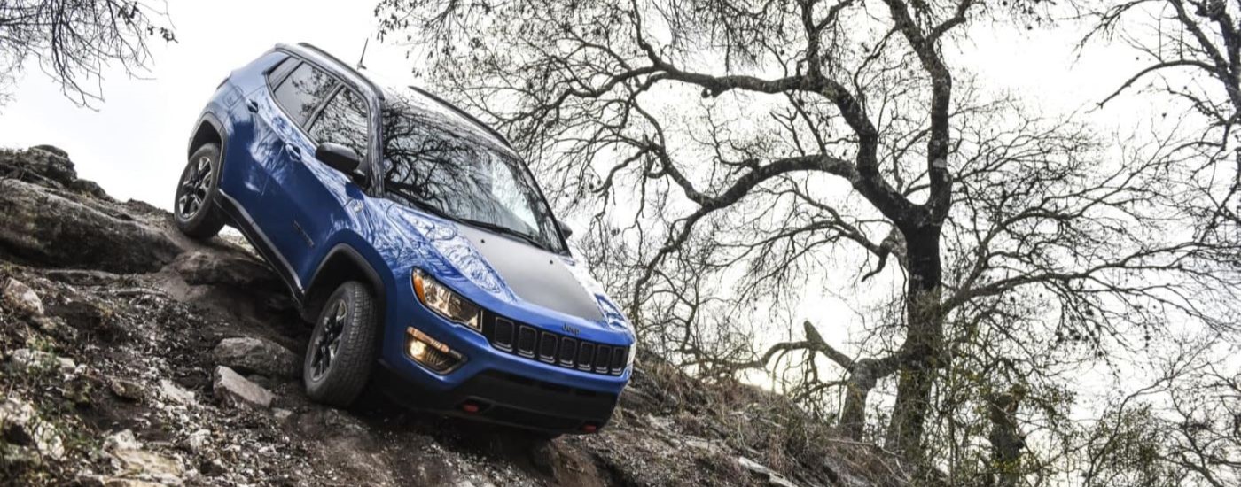 A blue 2021 Jeep Compass Trailhawk is shown crawling down a rocky hill.