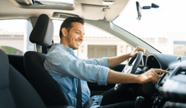 Smiling driver behind the wheel using the dashboard touchscreen