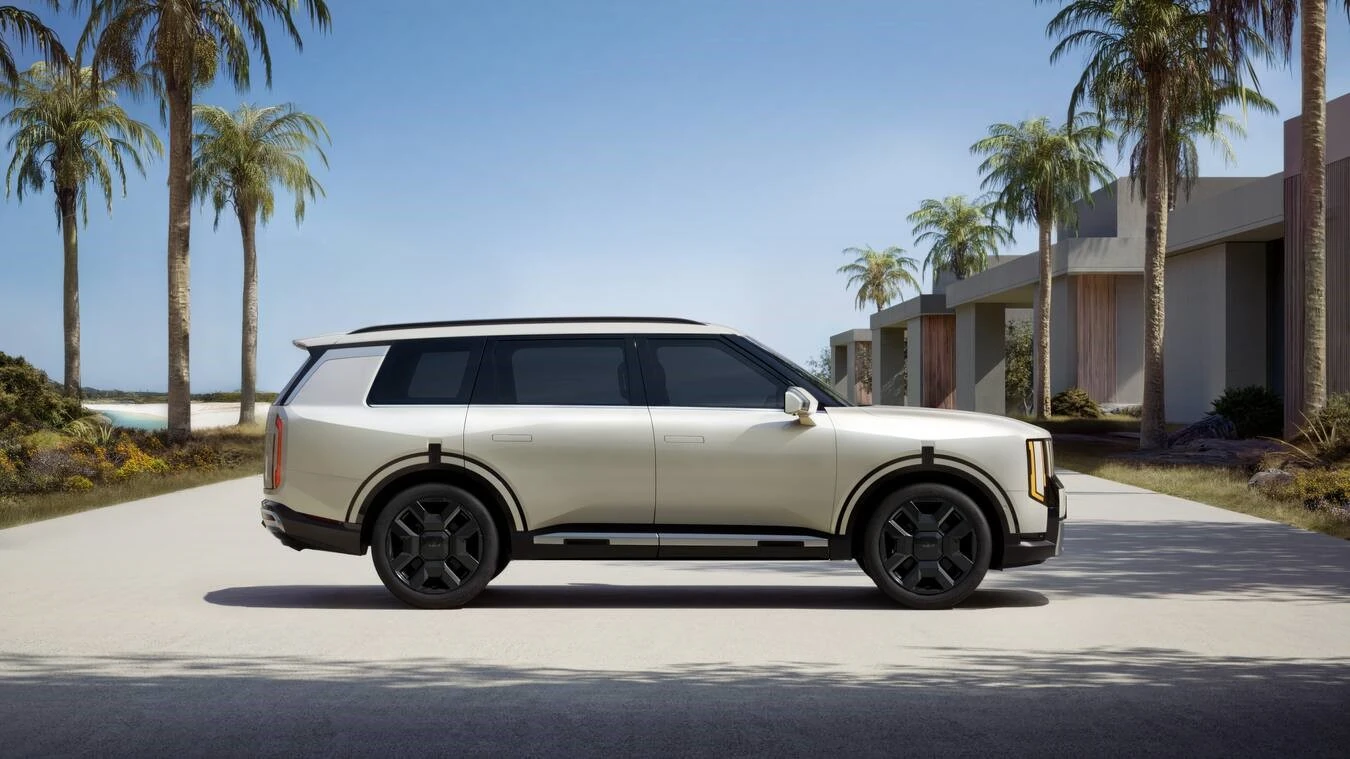 Champagne 2027 Kia Telluride HEV SXP shown in side profile, parked in a paved driveway with palm trees and a modern low-rise building behind it.