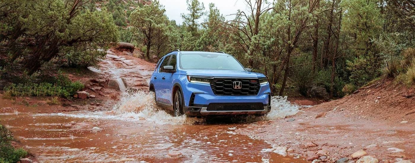 A blue 2023 Honda Pilot TrailSport driving through mud.